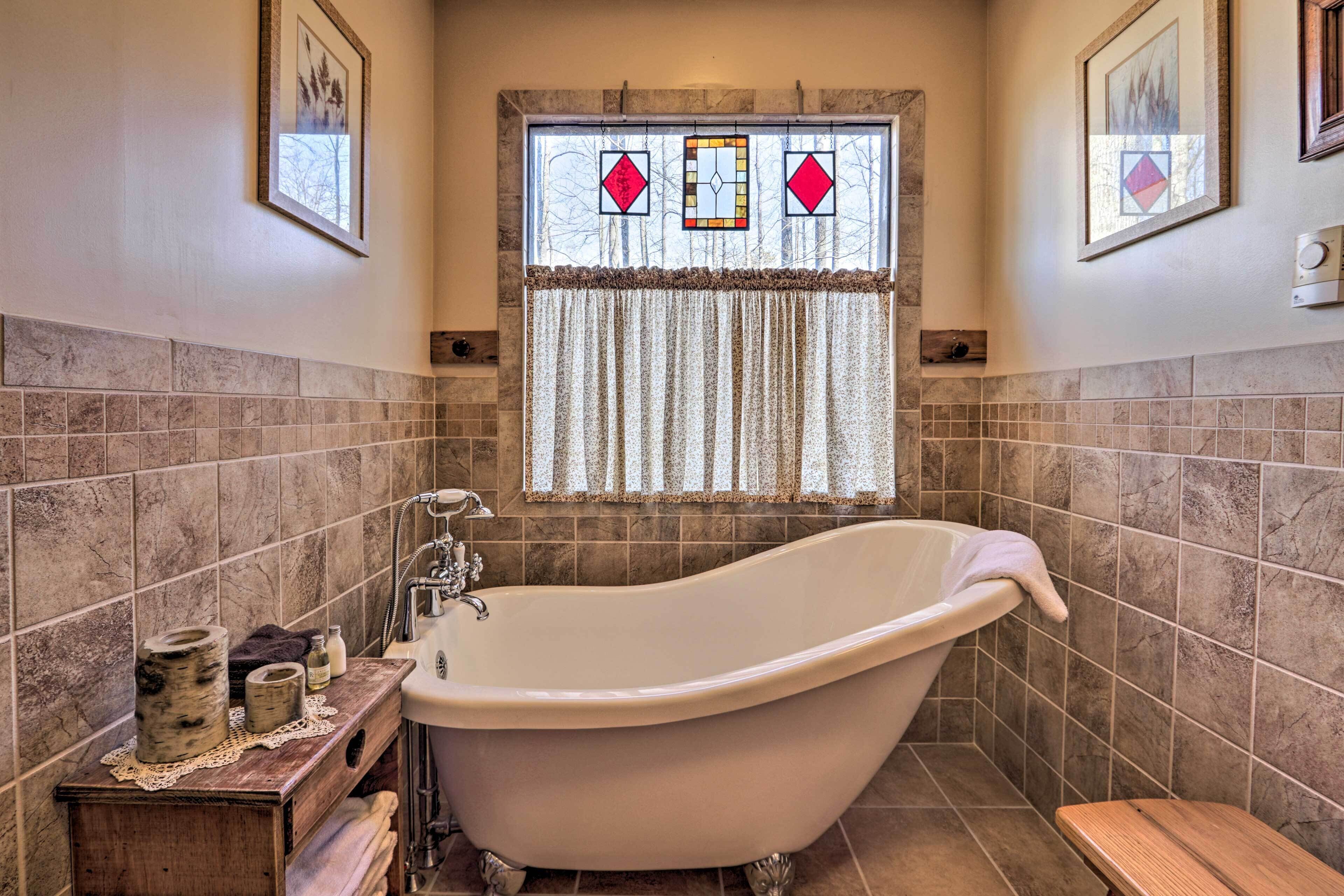 A bathroom with a freestanding bathtub, a wooden vanity, and a window with stained glass.