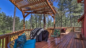 Um deck de madeira com pérgola, móveis de exterior e área coberta para churrasco.