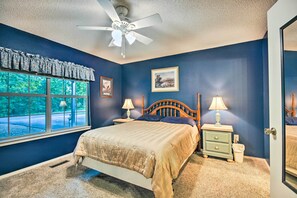 A bedroom with a bed, two bedside tables with lamps, a ceiling fan, a window with a view, and a door.