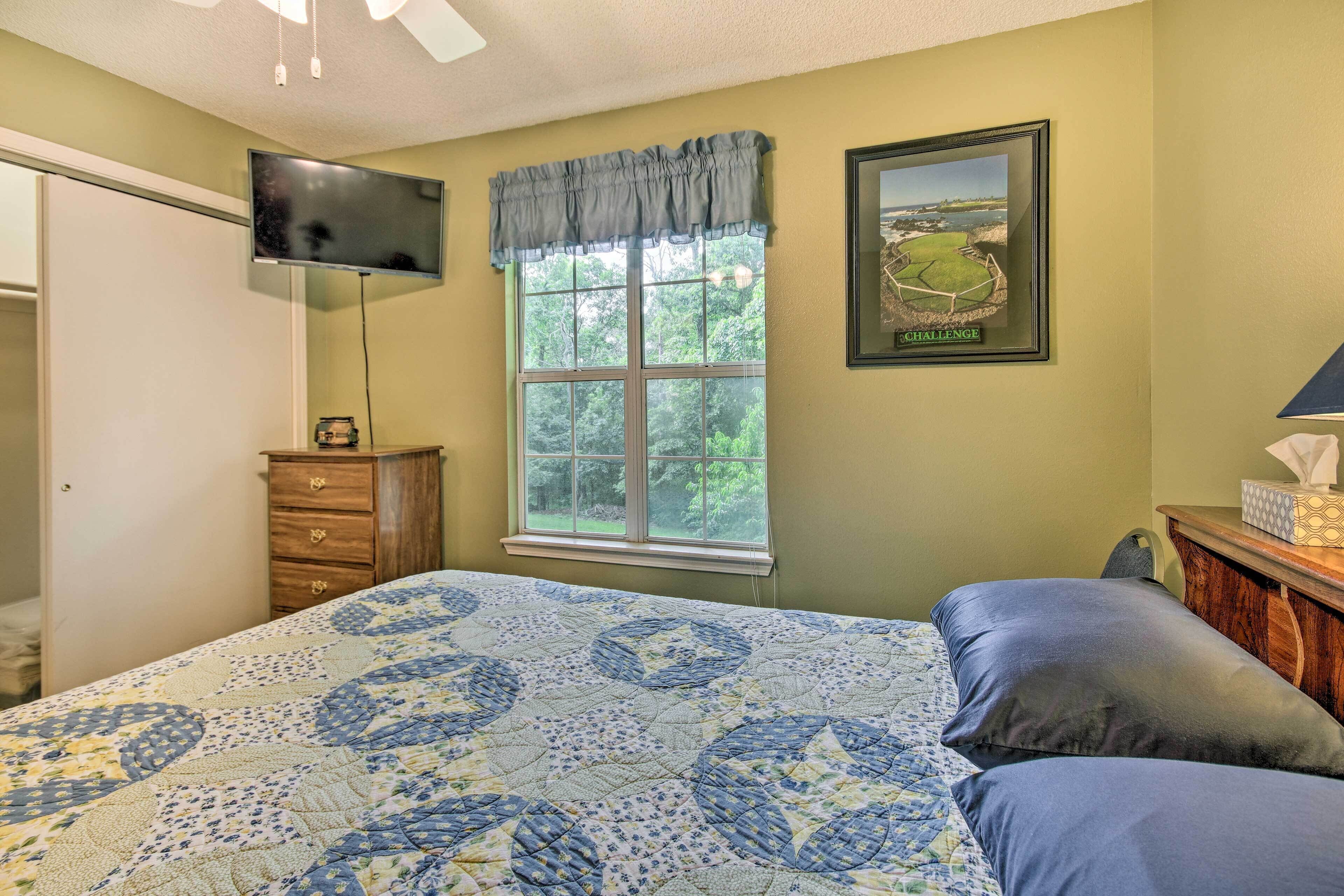 A bedroom with a bed, a dresser, a window, a television, and a framed picture on the wall.