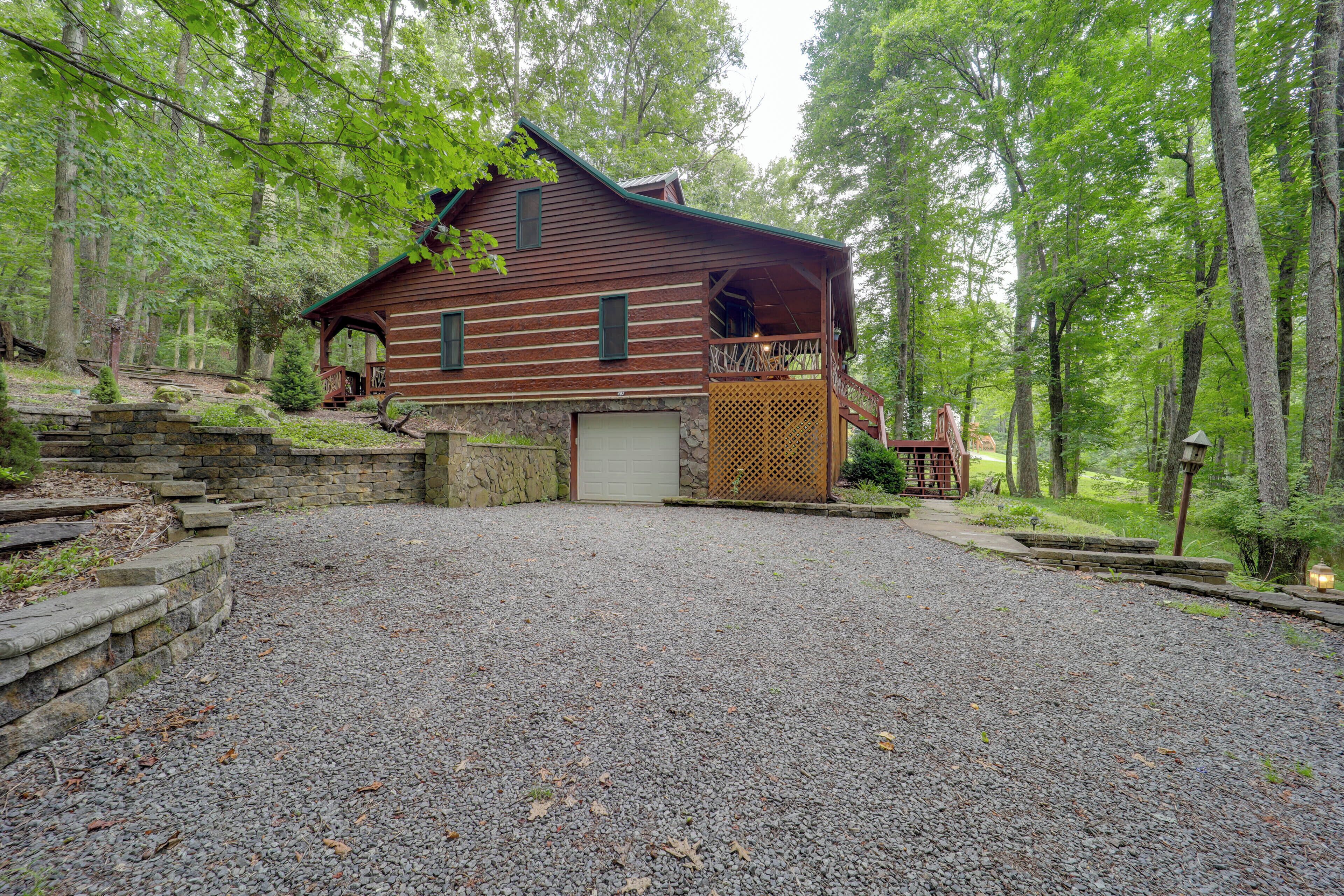 A rustic cabin with a stone foundation, a wooden deck, and a gravel driveway.