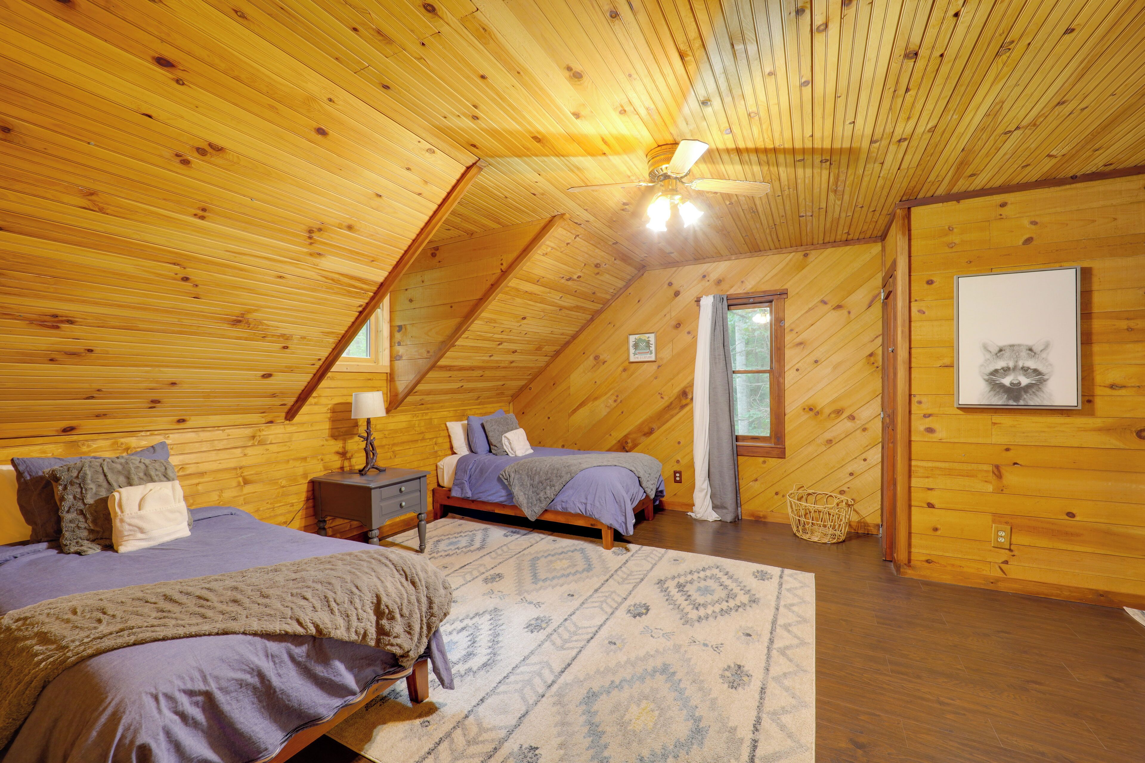 Ein gemütliches Schlafzimmer im Dachgeschoss mit Holzwänden und einer geneigten Decke, mit zwei Betten, einem Nachttisch, einer Lampe und einem gerahmten Bild an der Wand.