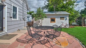 Eine Terrasse mit einem runden Metalltisch und Stühlen, ein kleines Gartenhaus und ein Fahrrad im Hintergrund.