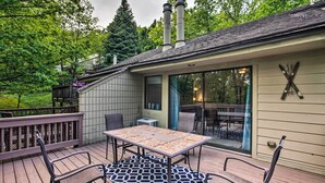 A covered outdoor deck with a table and chairs, a wooden railing, and a view of the surrounding greenery. - Cozy Wintergreen Resort Condo: Walk to Ski Lifts! (Roseland)
