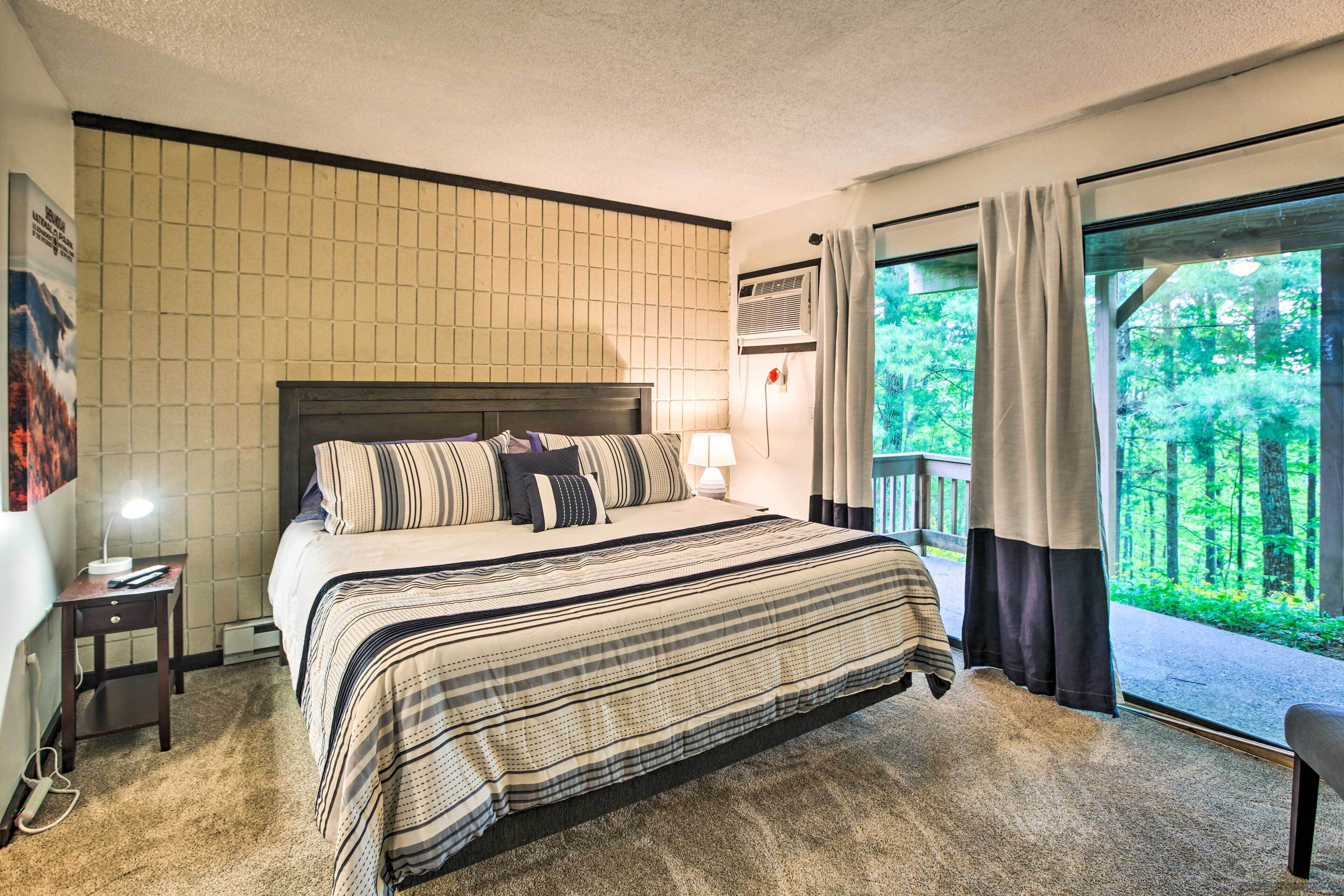 Une chambre d’hôtel avec un grand lit, une table de chevet, une lampe, une fenêtre avec des rideaux et une vue sur la verdure.