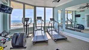 Une salle de sport équipée de tapis de course, d’un vélo d’appartement et d’un rameur, avec vue sur une plage.