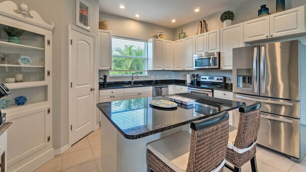 A modern kitchen with white cabinets, stainless steel appliances, and a central island with chairs.