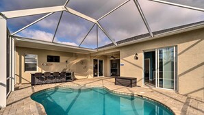 A swimming pool with a covered patio area, including a seating arrangement and a ceiling fan.