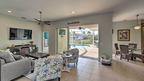 A spacious living room with a sofa, armchair, and coffee table, a dining area with chairs and a table, and a large sliding glass door leading to a pool area.
