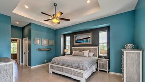 A bedroom with a bed, a ceiling fan, a nightstand, a dresser, and a painting on the wall.