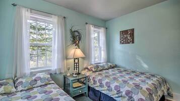 Un dormitorio con dos camas, una mesita de noche con lámpara y una ventana con cortinas.