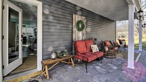 Une véranda couverte avec un coin salon doté de coussins rouges, une table en bois agrémentée de plantes et une porte donnant sur la cuisine.