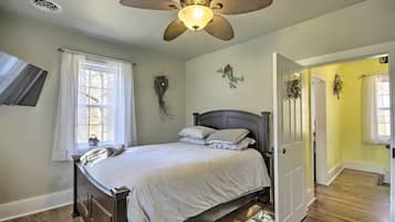 A bedroom with a bed, a ceiling fan, a TV, and a window with curtains.