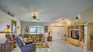 A spacious living room with a leather recliner, a TV on a wooden stand, and a large window.