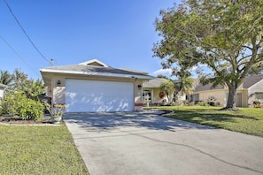 A single-story house with a garage, a well-maintained lawn, and a large tree in front. - Canal-view Home w/ Lanai in Cape Coral! (Cape Coral)