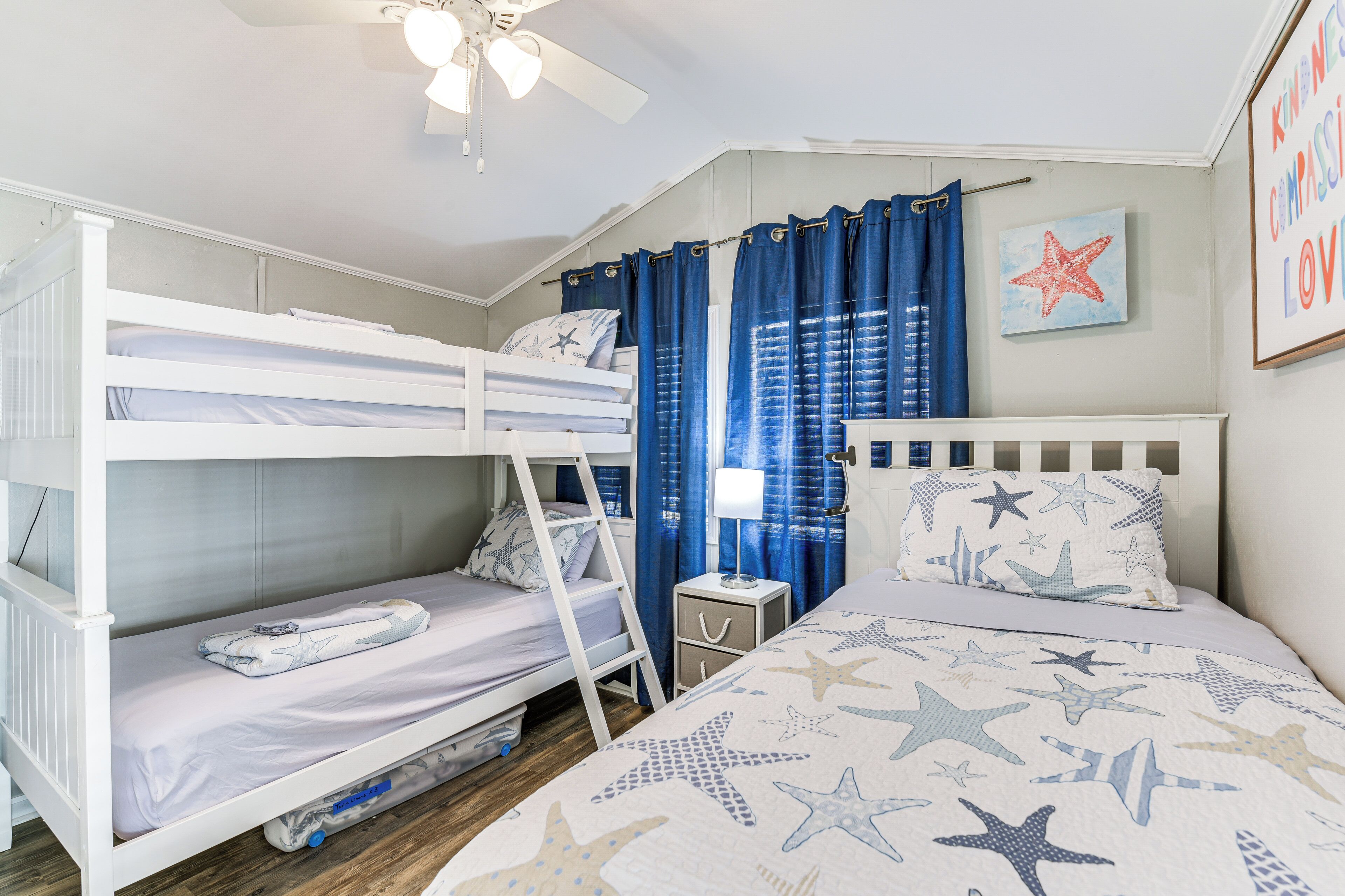 Une chambre avec un lit superposé, une échelle, une table de chevet avec une lampe et une literie sur le thème des étoiles.