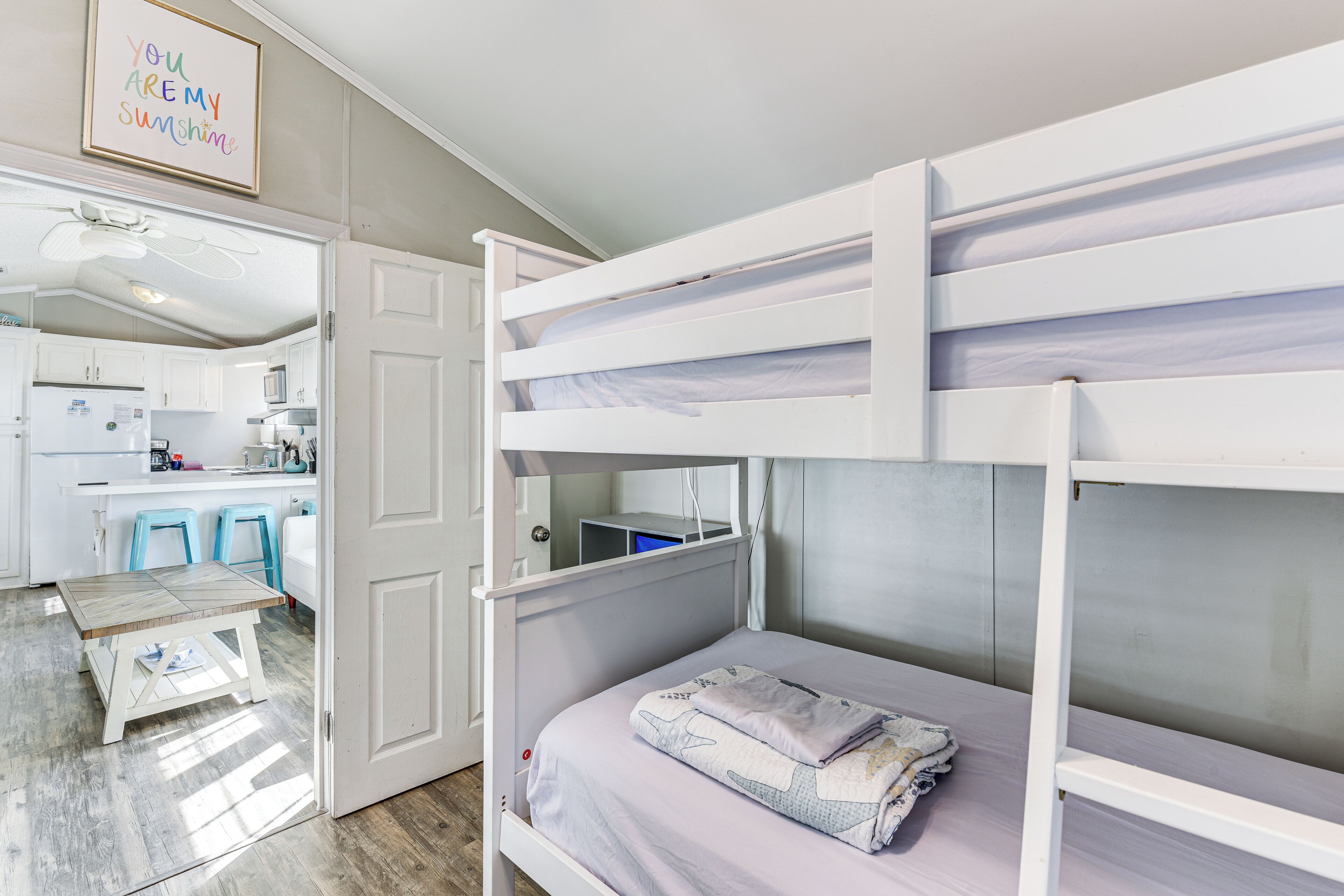 Une chambre avec des lits superposés, dont l’espace cuisine est visible à travers une porte ouverte.