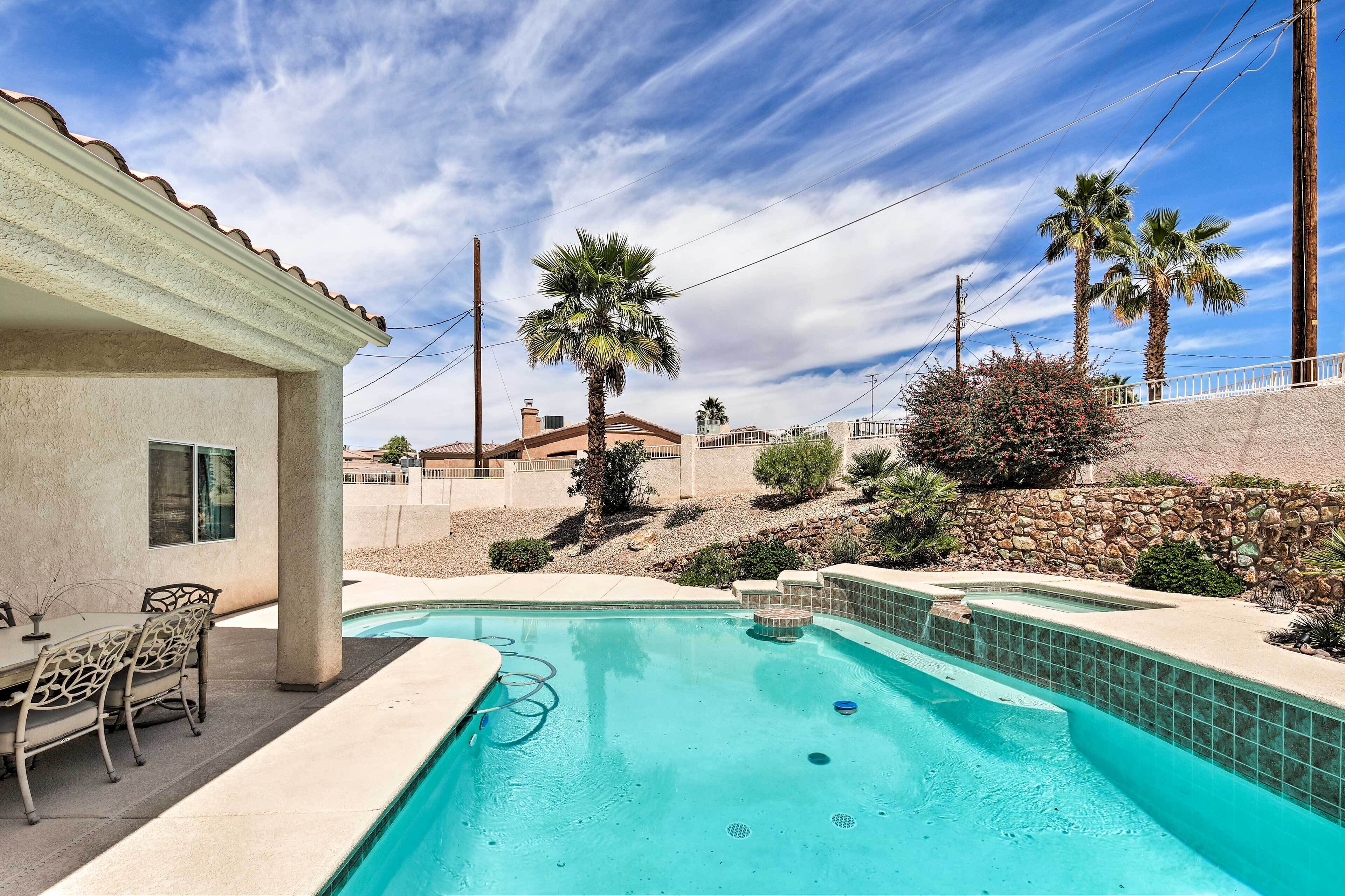 A swimming pool with a patio area, palm trees, and a stone wall.