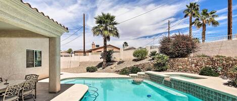 A swimming pool with a patio area, palm trees, and a stone wall.