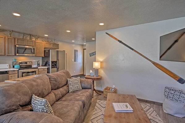 A modern living room with a brown leather sofa, a wooden coffee table, and a kitchen area with wooden cabinets and a microwave. - Charming Home - 1 Mi to Yellowstone National Park! (West Yellowstone)