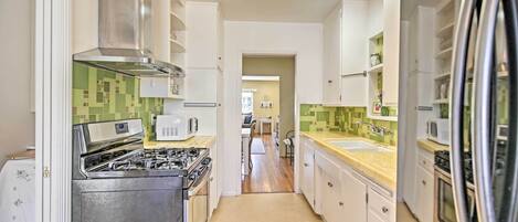 Una cocina moderna con armarios blancos, electrodomésticos de acero inoxidable y un salpicadero de azulejos verdes.