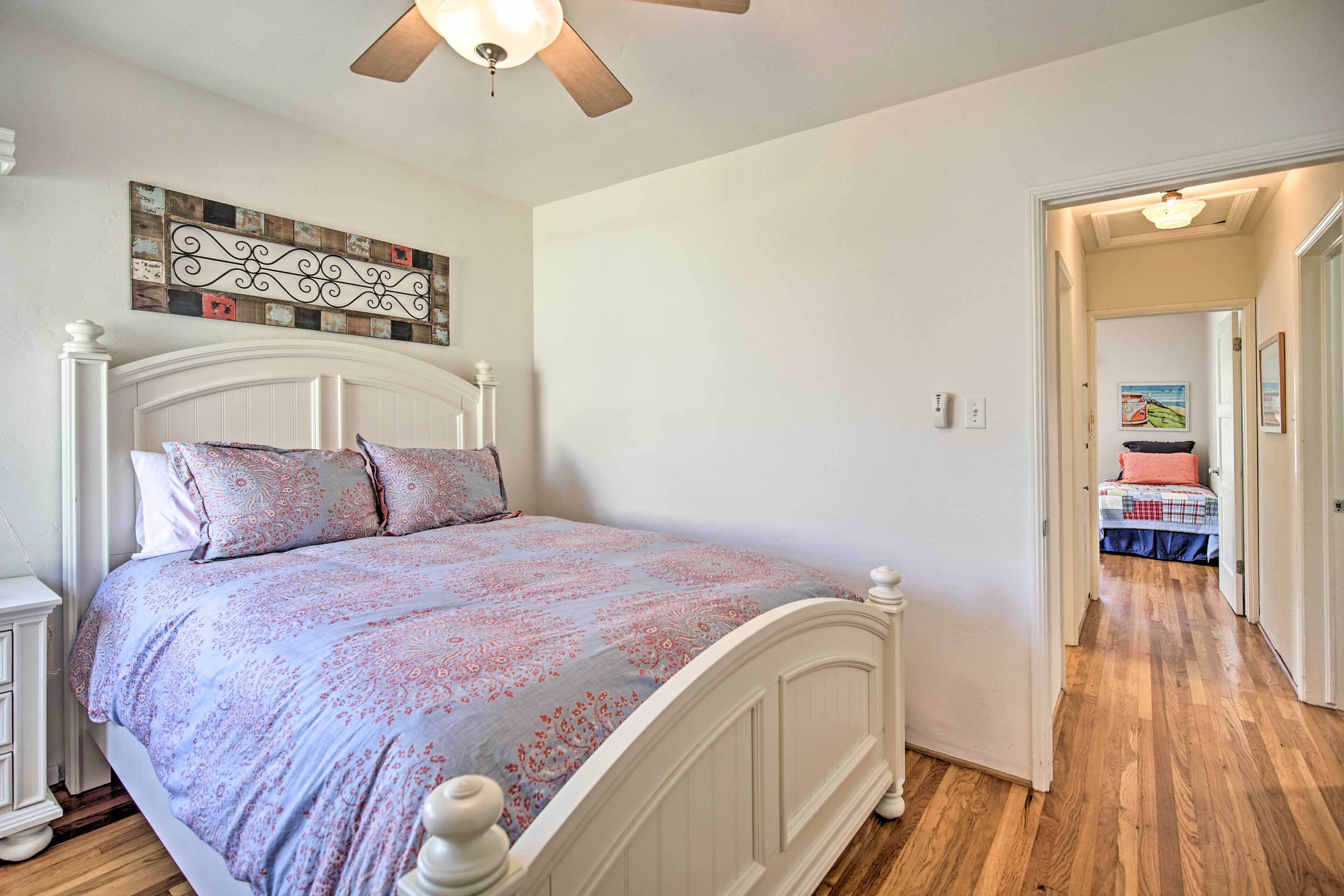 Un dormitorio con una cama blanca, un ventilador de techo y piso de madera.