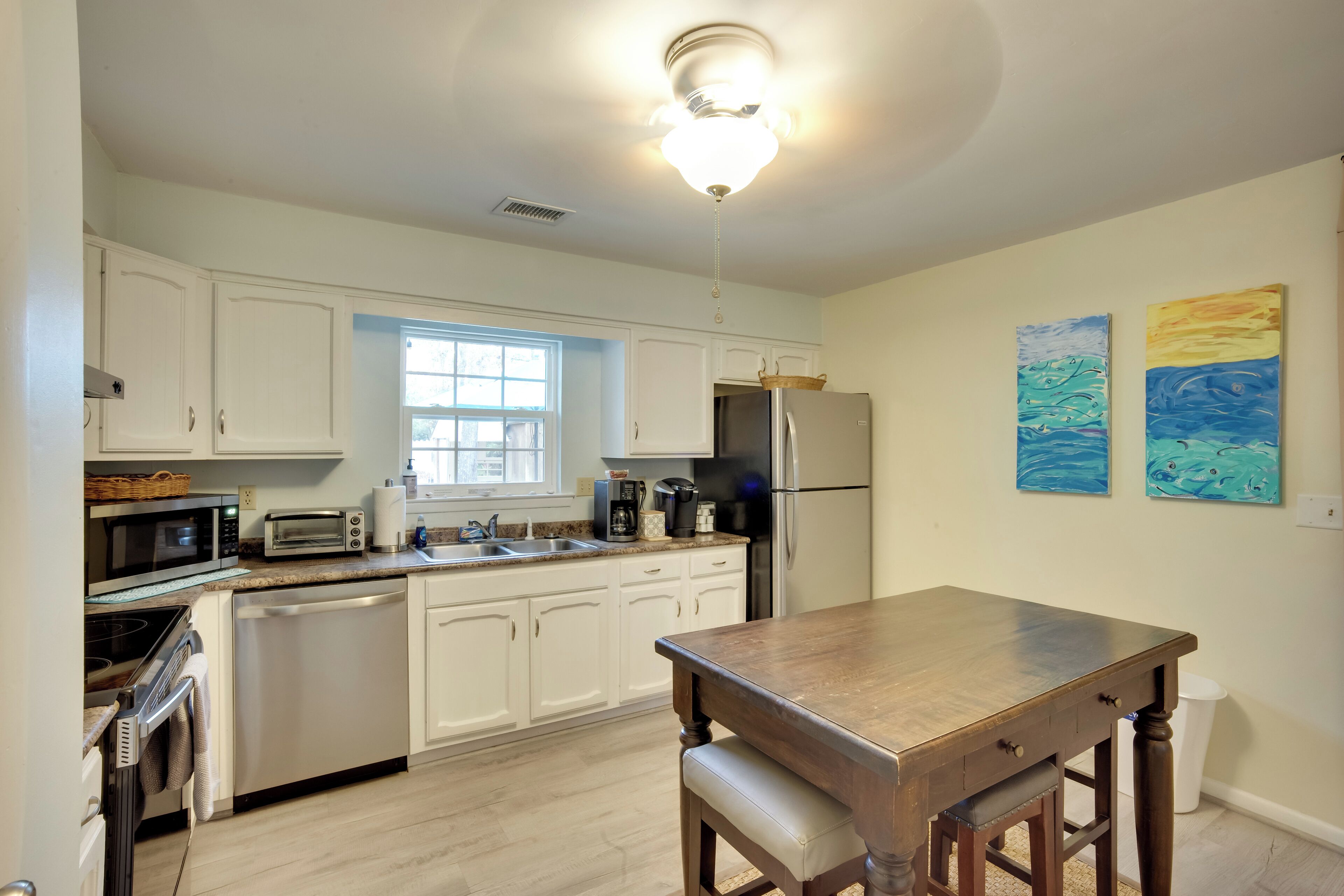 A modern kitchen with white cabinets, a wooden dining table, and a ceiling fan.