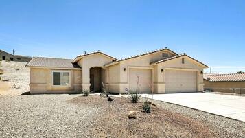 A single-story house with a garage, a small front porch, and a gravel driveway.