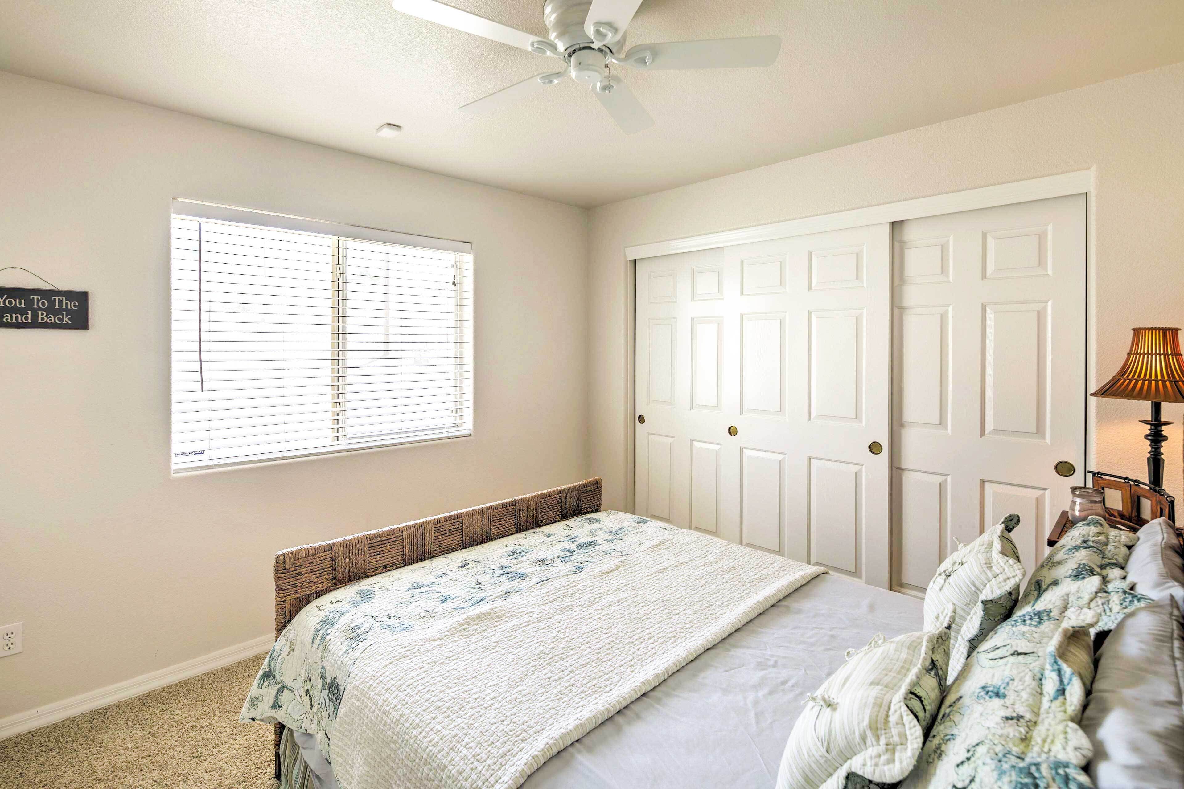 Ein Schlafzimmer mit Bett, Deckenventilator, Fenster mit Jalousien, Tür und Lampe.