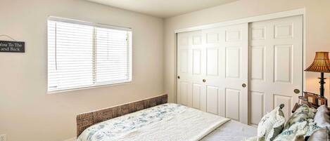 Ein Schlafzimmer mit Bett, Deckenventilator, Fenster mit Jalousien, Tür und Lampe.