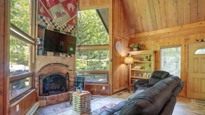 A cozy cabin interior with a fireplace, leather sofa, wooden walls, and large windows.
