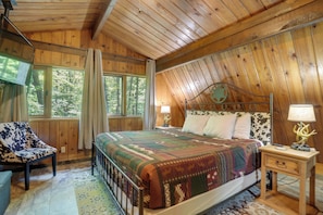 A wooden cabin bedroom with a bed, a chair, a nightstand, and a window. - Cozy Cabin Near Massanutten Resort & Water Park! (McGaheysville)