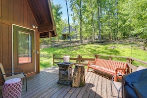 A wooden deck with outdoor seating, a stone fire pit, and a view of a forested area. - Cozy Cabin Near Massanutten Resort & Water Park! (McGaheysville)