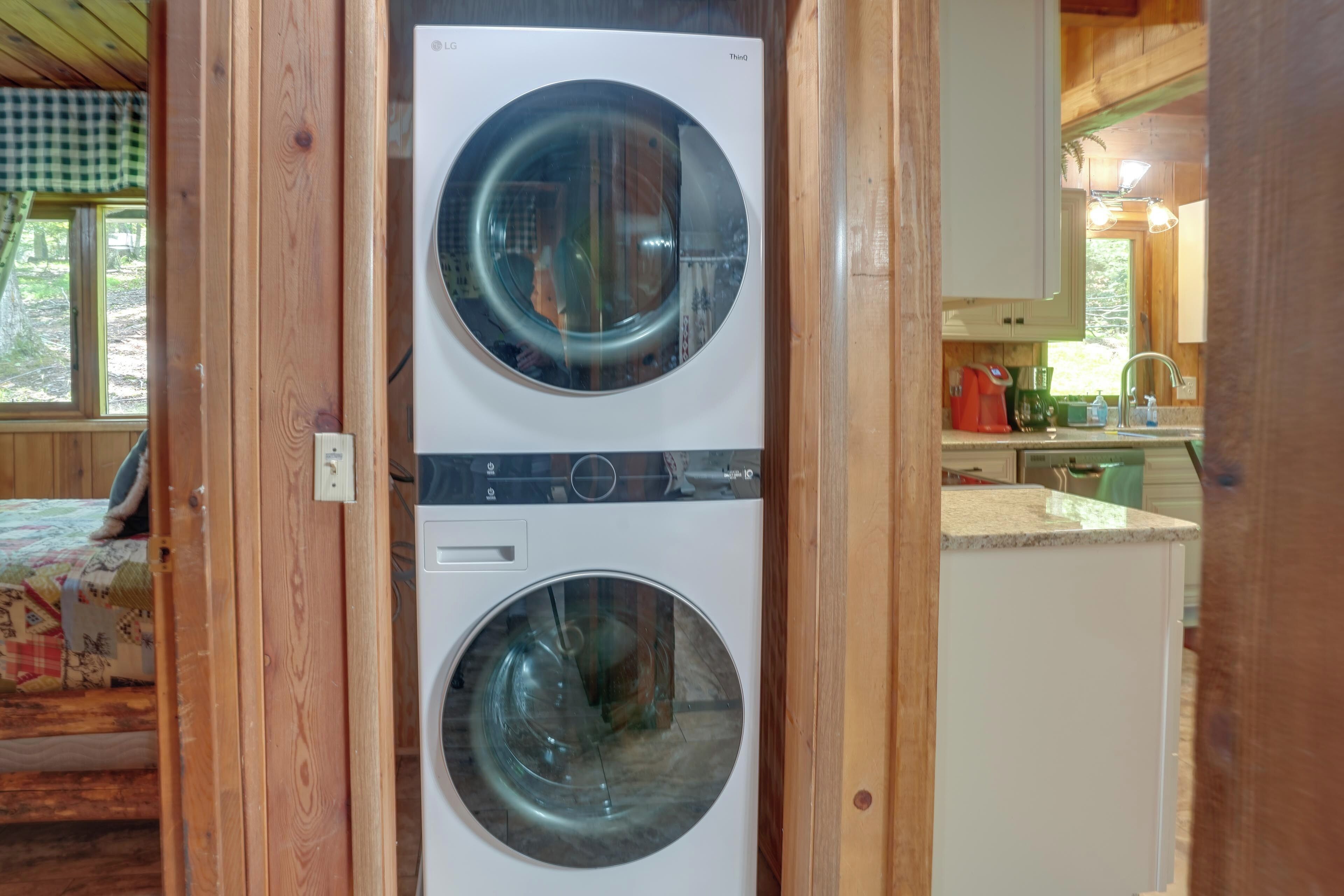 A laundry room with two front-loading washing machines, wooden walls, and a kitchen area visible through an open door.