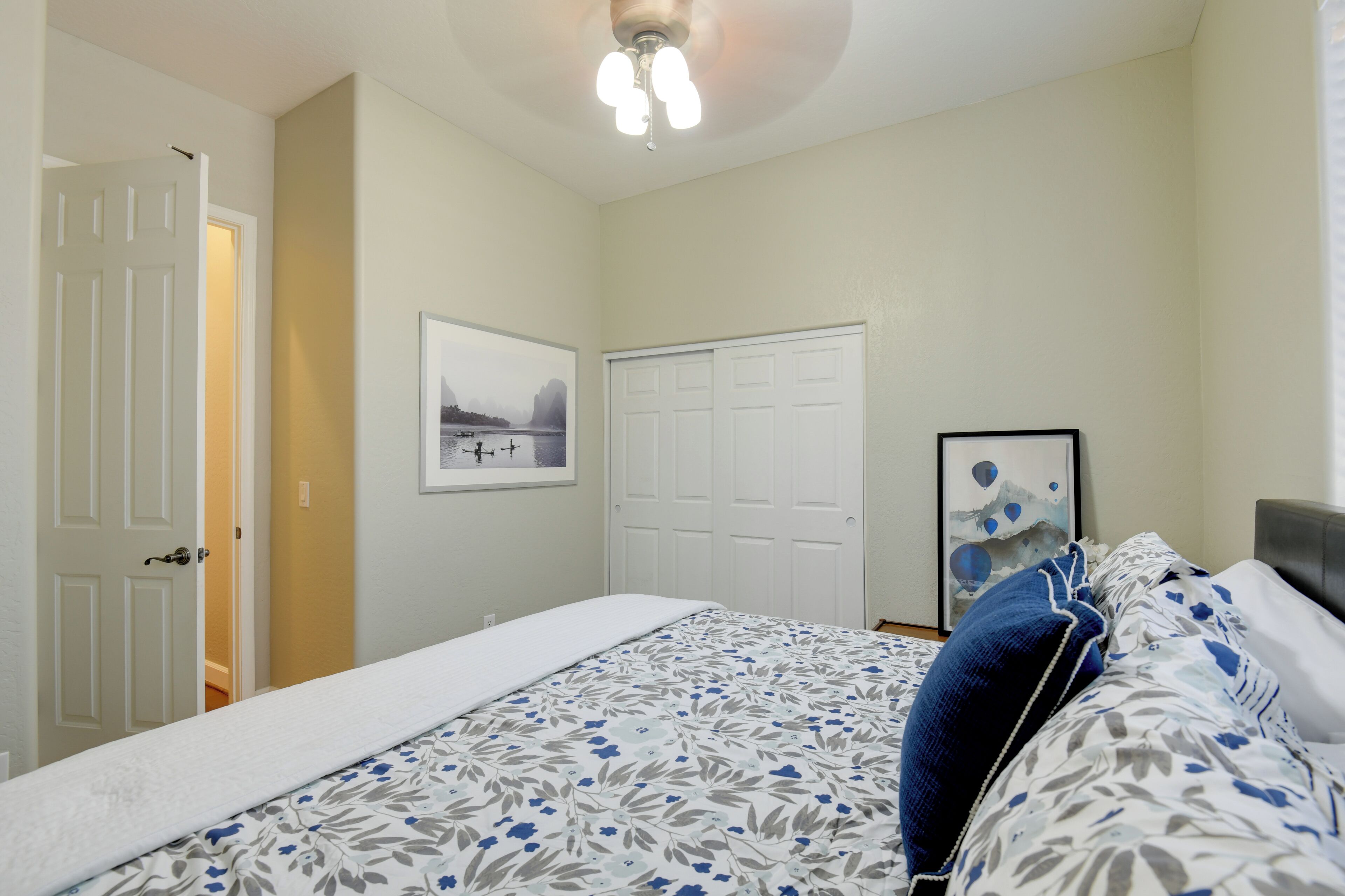 Quarto com uma cama, porta, ventilador de teto e um quadro na parede.
