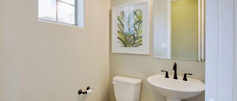 A bathroom with a toilet, sink, and a framed plant on the wall.