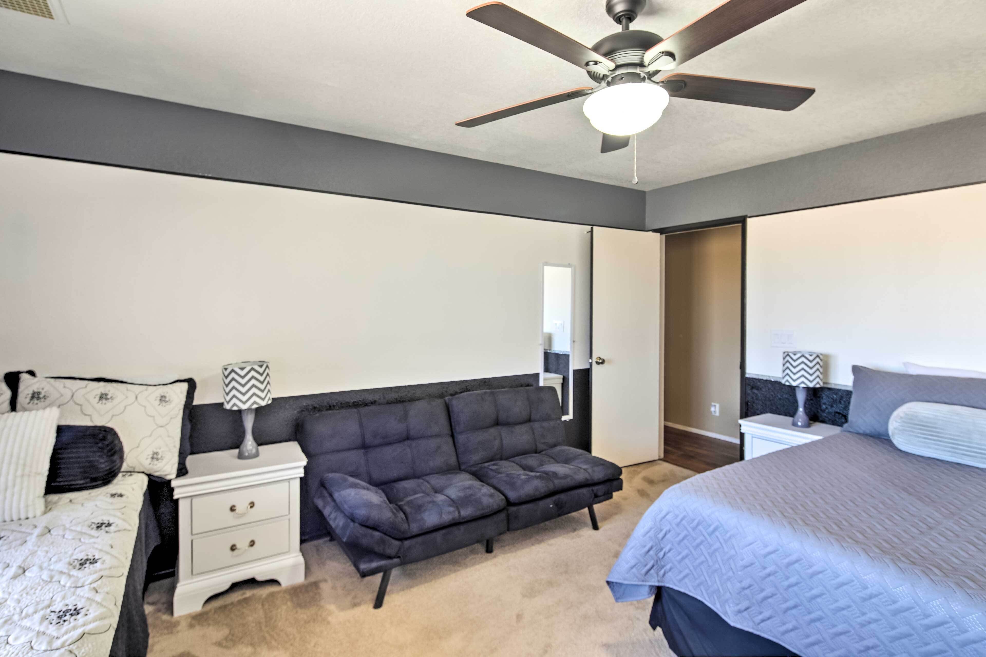 Une chambre à coucher comprenant un lit, un canapé, une table de chevet, un ventilateur de plafond et une porte.