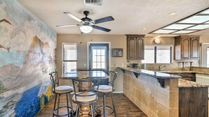 A modern kitchen with a central island, bar stools, a ceiling fan, and a mural on the wall. - Bullhead City Home w/ Private Pool, Hot Tub & View (Bullhead City)