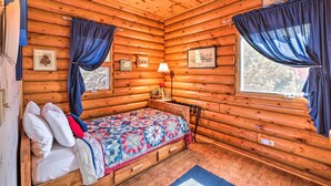 Ein gemütliches Schlafzimmer in einer Blockhütte mit einem Bett, einem Nachttisch, einer Lampe und gerahmten Bildern an den Wänden.
