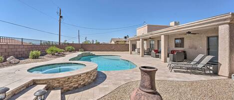 A backyard with a swimming pool, a patio area with lounge chairs, and a large decorative vase.