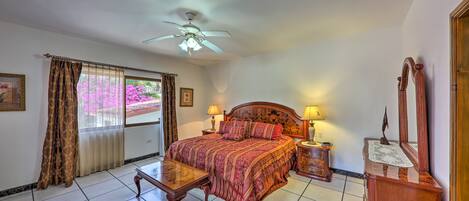 A bedroom with a bed, bedside tables, a ceiling fan, a window with curtains, and a wooden dresser.