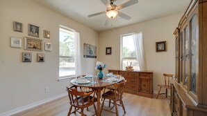 A dining area with a wooden table set for four, surrounded by wooden chairs. There is a ceiling fan above the table, and a wooden cabinet with drawers to the right.