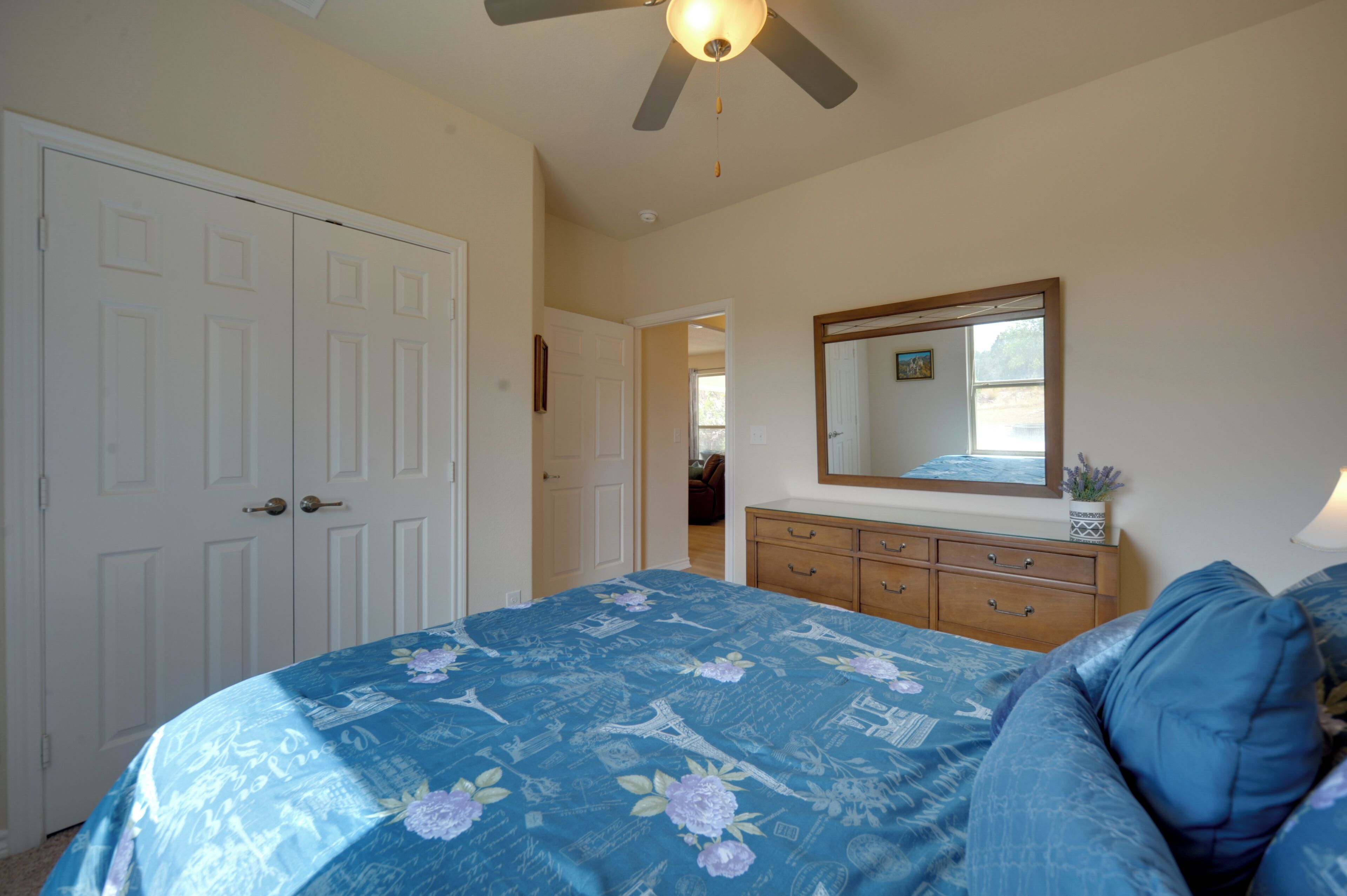 A bedroom with a bed, a dresser, a ceiling fan, and a mirror.
