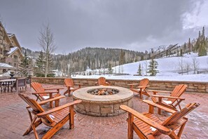 A fire pit surrounded by wooden Adirondack chairs in an outdoor setting with a view of a snowy mountain and trees. - Luxe Montage Deer Valley Retreat: Ski-in/ski-out! (Park City)