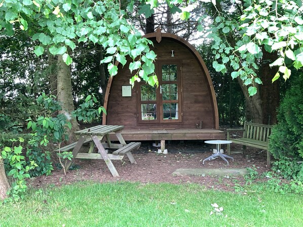 A wooden cabin with a large window, a picnic table, and a bench. - Woodland Camping pod With use of Campsite Bathroom (Grantham)