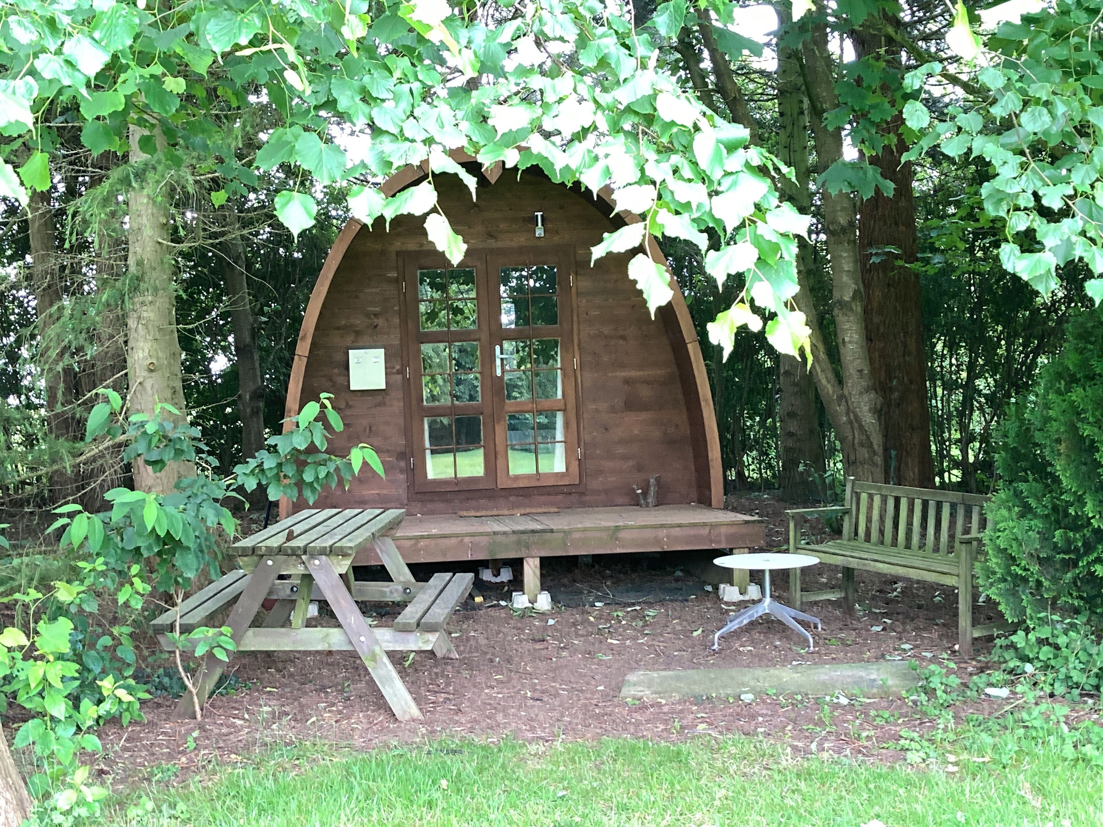 Une cabane en bois dotée d’une grande fenêtre en arc de cercle, d’une table de pique-nique et d’un banc.