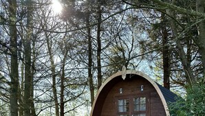 A wooden cabin with a curved roof, a bench, and a picnic table in a forest setting. - Woodland Camping pod With use of Campsite Bathroom (Grantham)