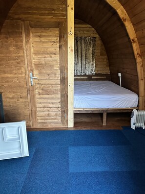 A wooden room with a bed, a radiator, and a blue carpet. - Woodland Camping pod With use of Campsite Bathroom (Grantham)