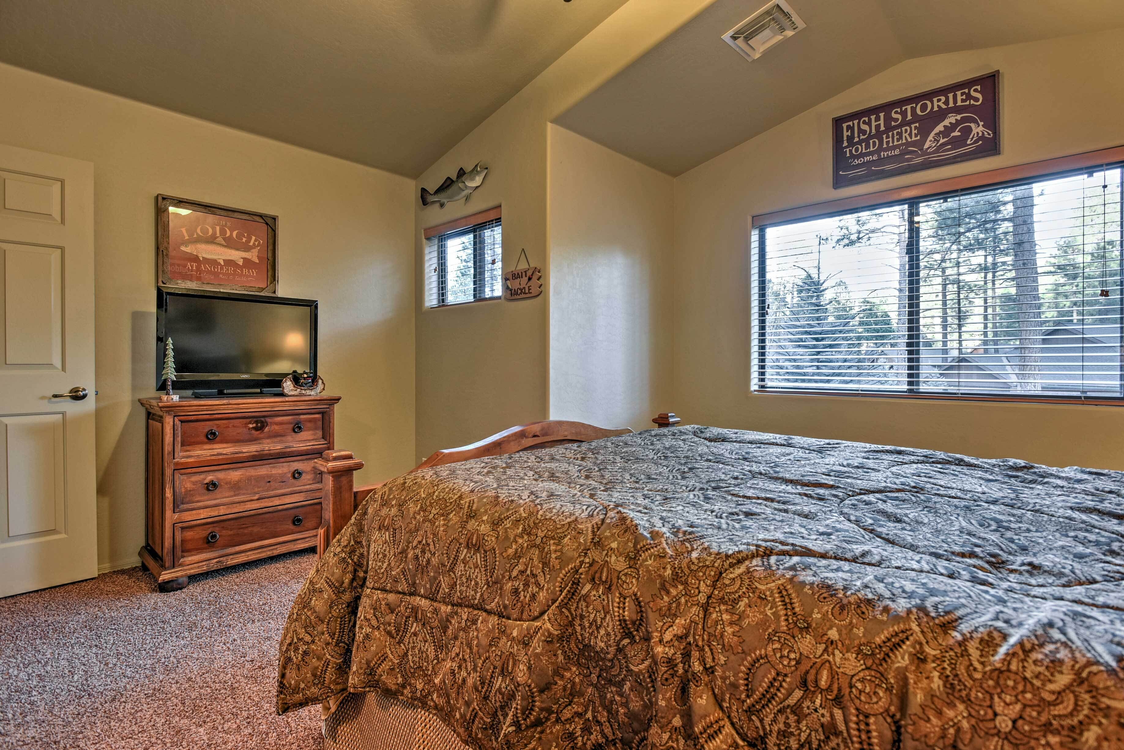 A bedroom with a bed, dresser, television, and a window with blinds.
