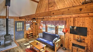 L’intérieur chaleureux d’un chalet avec un plafond en bois, un canapé, un téléviseur et une cheminée.